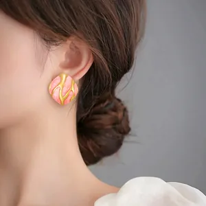 Détail des boucles d'oreilles irrégulières en résine rose aux motifs artistiques dorés