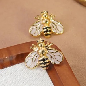 Détail macro de boucles d'oreilles abeille avec monture dorée et ailes en émail blanc