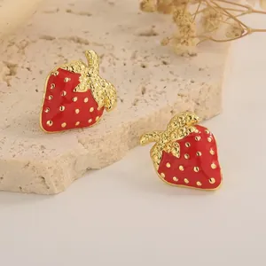 Dettaglio degli orecchini a fragola in smalto rosso con foglie dorate su pietra chiara