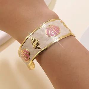 Dettaglio del bracciale dorato con conchiglie in smalto rosa e design marino sul braccio