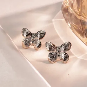 Detailed view of silver butterfly stud earrings with fine textured wings on white silk