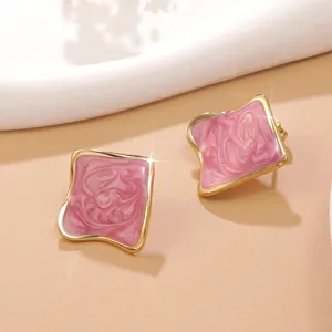 Boucles d'oreilles carrées marbrées roses avec bordure dorée sur fond minimaliste