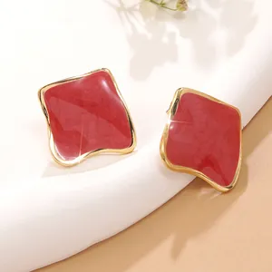 Détail de boucles d'oreilles carrées en émail rouge avec bords dorés irréguliers