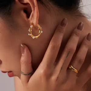 Dettaglio di orecchini a cerchio in oro 18K con perle e anello a onde con strass su modella