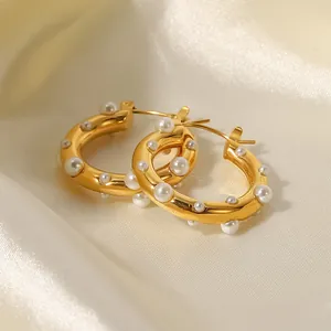 Eleganti orecchini a cerchio in oro 18K con perle bianche su una superficie di raso