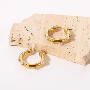 Eleganti orecchini a cerchio placcati oro 18K con perle bianche su sfondo in pietra