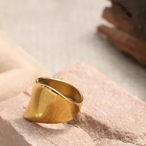 Dettaglio di anello largo dorato con bordi ondulati irregolari e finitura lucida a specchio