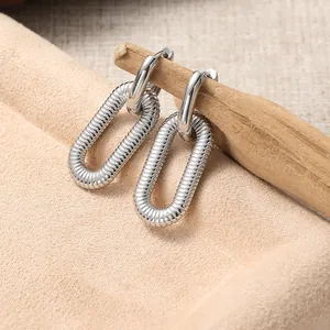 Makro-Detail silberner Gliederohrringe mit ovalem strukturiertem Anhänger auf Holz