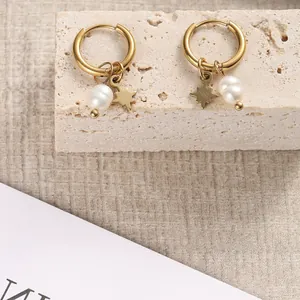 Detailansicht goldener Creolen mit Perlen und Sternanhängern auf einer Steinfläche