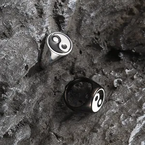 Detailed view of silver and black stainless steel Yin Yang rings on a dark rock surface