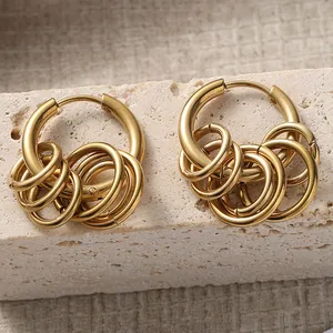 Golden multi-layer hoop earrings with five small dangling rings on a textured stone surface