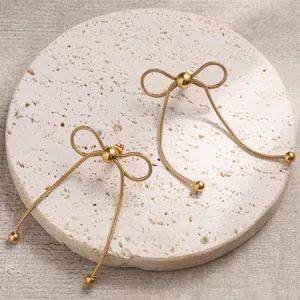 Detail of golden bow-knot tassel earrings made of flat snake chains on a stone base