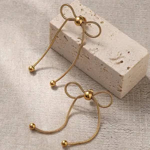 Elegant gold bow earrings with snake chain tassels displayed on an aesthetic stone base