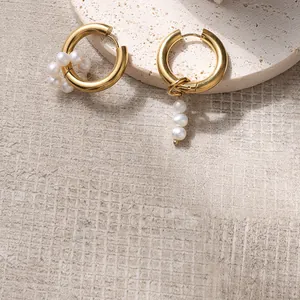 Macro detail of asymmetric gold earrings with freshwater pearls on a stone tray