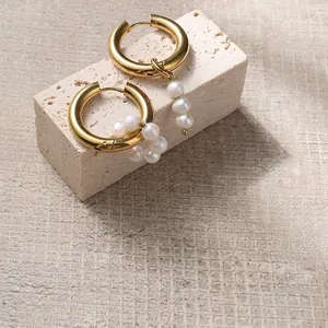 Macro detail of asymmetric gold hoop earrings featuring elegant freshwater pearl pendants