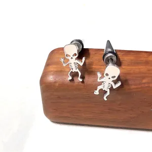 Détail de boucles d'oreilles tête de mort en acier inoxydable sur présentoir en bois