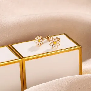 Detailed macro of golden daisy stud earrings with white enamel petals on silk background