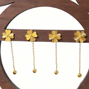 Golden clover drop earrings with laser heart texture and bead chains on wood stand