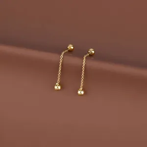 Macro shot of gold tassel drop earrings with small beads and delicate chains on brown backdrop