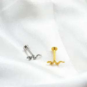 Macro-opname van zilveren en gouden slang labret piercings op witte zijden stof