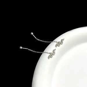 Macro detail of silver stainless steel snake threader earrings on a white ceramic plate