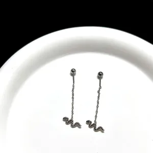 Detailed macro view of silver snake-shaped drop earrings with delicate chain on a white tray