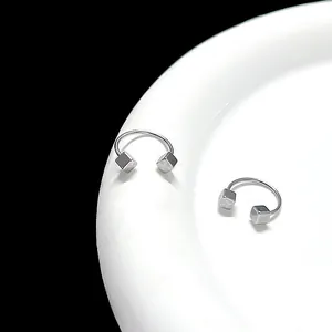 Macro shot of silver U-shaped earrings with geometric cubes on a ceramic plate