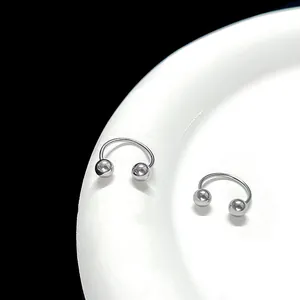 Macro view of bright silver horseshoe piercing rings with spheres on a white ceramic edge