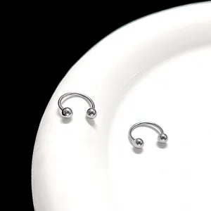 Macro shot of silver horseshoe rings with screw balls on a white plate with black background