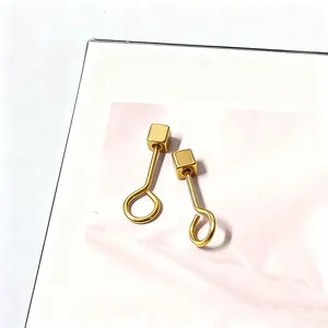 Detail van minimalistische vergulde titanium stalen oorbellen met kleine geometrische kubussen