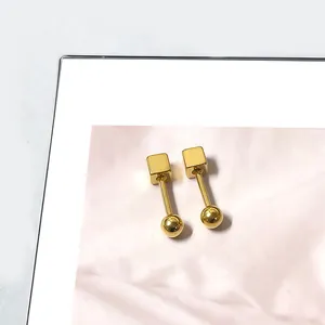 Macro-opname van geometrische gouden kubusoorbellen met ronde bolsluiting en glanslak