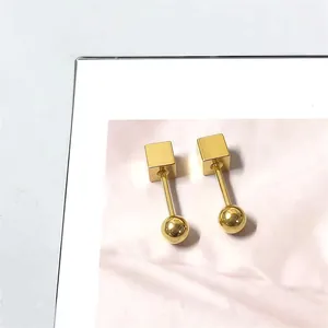 Detailopname van gouden geometrische oorbellen met kubus en bol op roze marmeren kaart