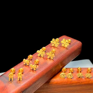 Nahaufnahme goldener Ohrstecker mit Schleifen- und Blumenmotiven auf dunklem Holzständer