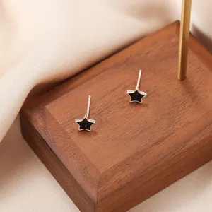 Close-up of geometric black enamel star stud earrings on champagne silk fabric