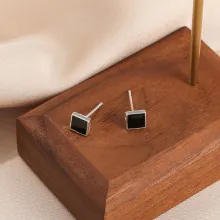 Close-up of square black enamel stud earrings with S925 silver frame on wood display
