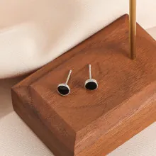 Detail of silver round stud earrings with black enamel inlay on dark wood surface
