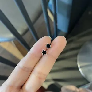 Close-up of minimalist black star stud earrings with silver borders held by fingers