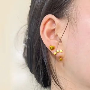 Primer plano de pendiente de corazón y tres estrellas doradas pulidas en la oreja
