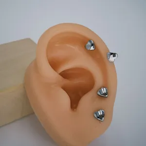 Detailed view of four mini silver heart stud earrings shown on a silicone ear model