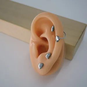 Detail showing small silver heart stud earrings worn on a silicone ear model for size