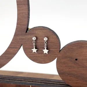 Detail of star-shaped titanium steel drop earrings with spherical studs on wooden stand