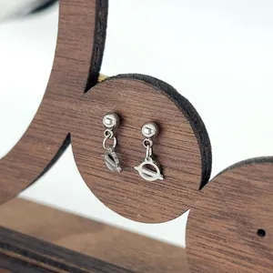 Close-up of geometric silver stainless steel drop earrings on a wooden jewelry display stand