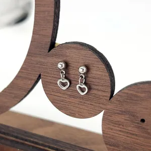 Detailed close-up of silver steel stud earrings featuring a hollow heart dangle design
