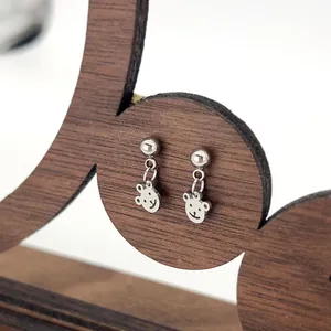 Detailed view of silver bear-shaped earrings hanging on a wooden jewelry display stand