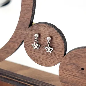 Detailed shot of titanium steel stud earrings featuring a hollow butterfly charm on wood