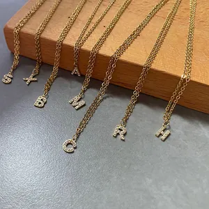 Close-up of gold snake chain necklaces with crystal-encrusted alphabet pendants on wood