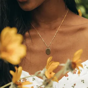 Elegante goldene Halskette mit ovalem Anhänger für Damen, getragen in sonniger Kulisse