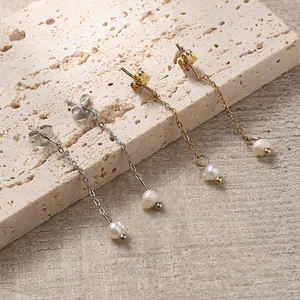 Elegant gold and silver long chain freshwater pearl drop earrings on a stone display