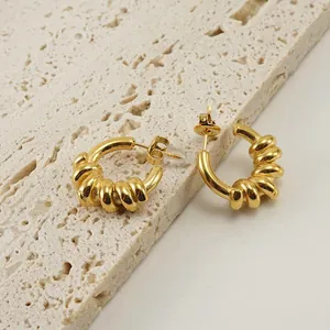 Elegante 18K vergoldete Edelstahl-Creolen in gedrehter Form auf Stein-Hintergrund