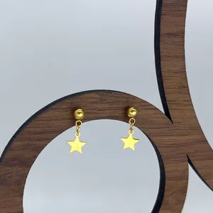 Λεπτομερής κοντινή λήψη χρυσών σκουλαρικιών αστεριών από ατσάλι τιτανίου σε ξύλινη βάση